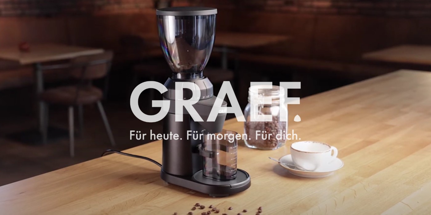 Macinacaffè con chicchi di caffè e tazza su un tavolo di legno. GRAEF.