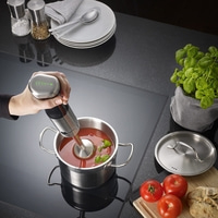 Personne mélangeant une soupe de tomates avec un mixeur plongeant dans une casserole.