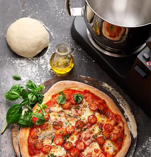 Pizza con ingredienti, impasto, olio e mixer sul tavolo