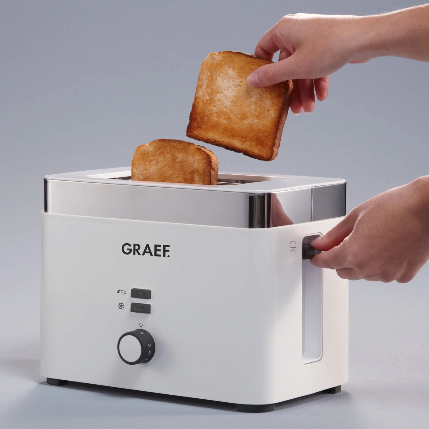 White toaster with toast, hands operating the appliance, bread.