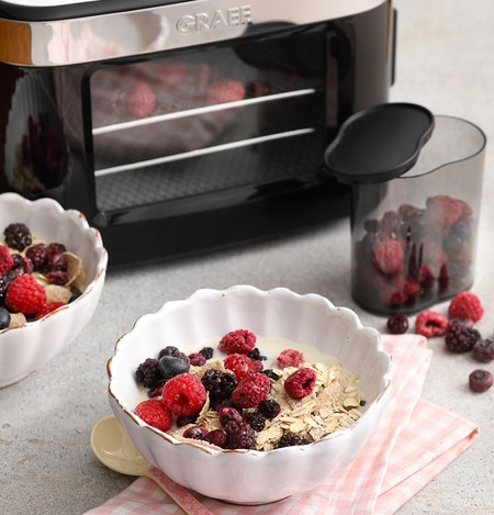 Breakfast with berries and cereal, next to a dehydrator and container.