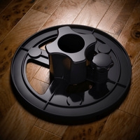 Objet noir sur bois. Base ronde avec boutons et un trou central. Surface brillante.