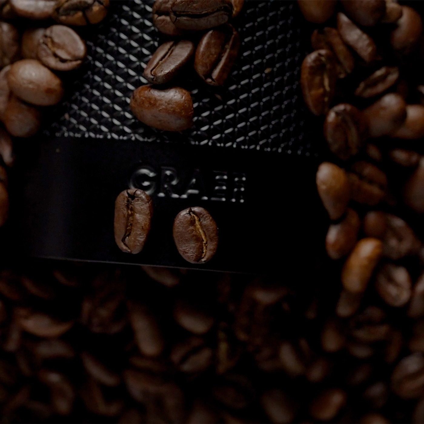 Chicchi di caffè tostati circondano un macinacaffè con il logo GRAEF.