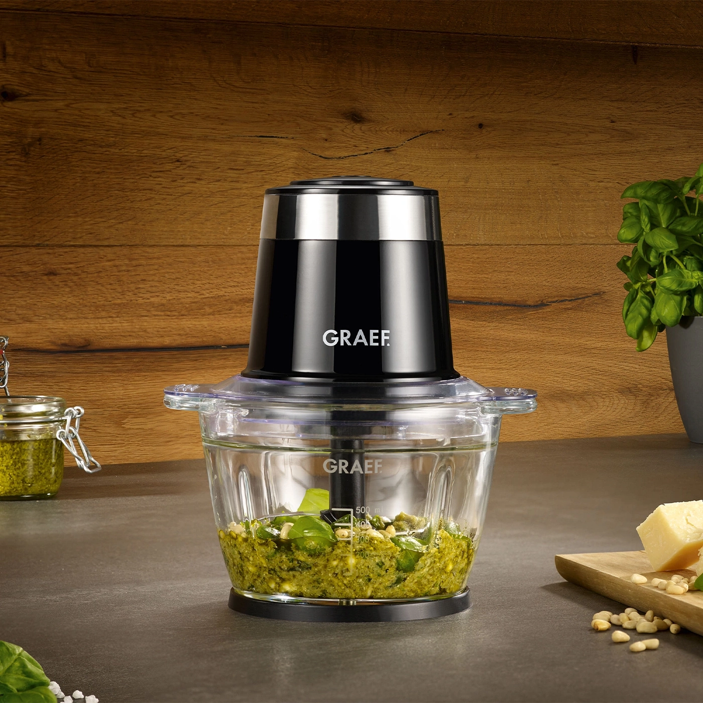 Food processor with pesto, cheese, and pine nuts on a table