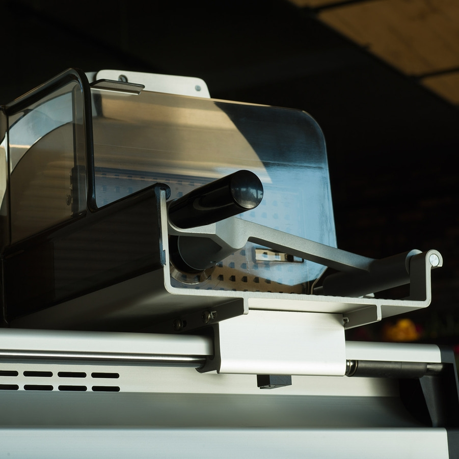 Close-up of a professional metal meat slicer with a black handle and a clear guard