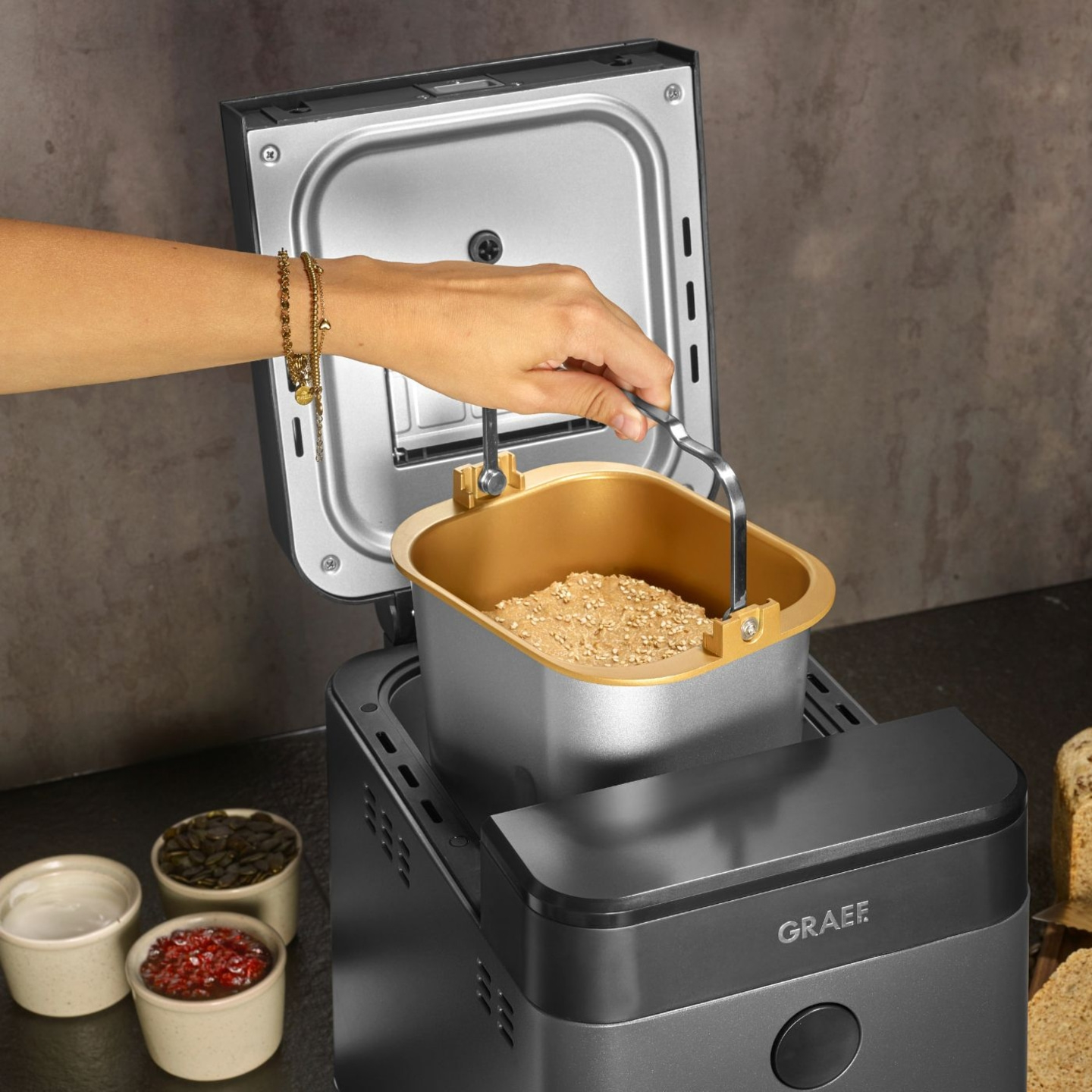 Macchina per il pane con ingredienti e mano che tiene il contenitore, primo piano