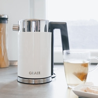 Bouilloire blanche avec une tasse de thé et des biscuits sur un comptoir de cuisine.