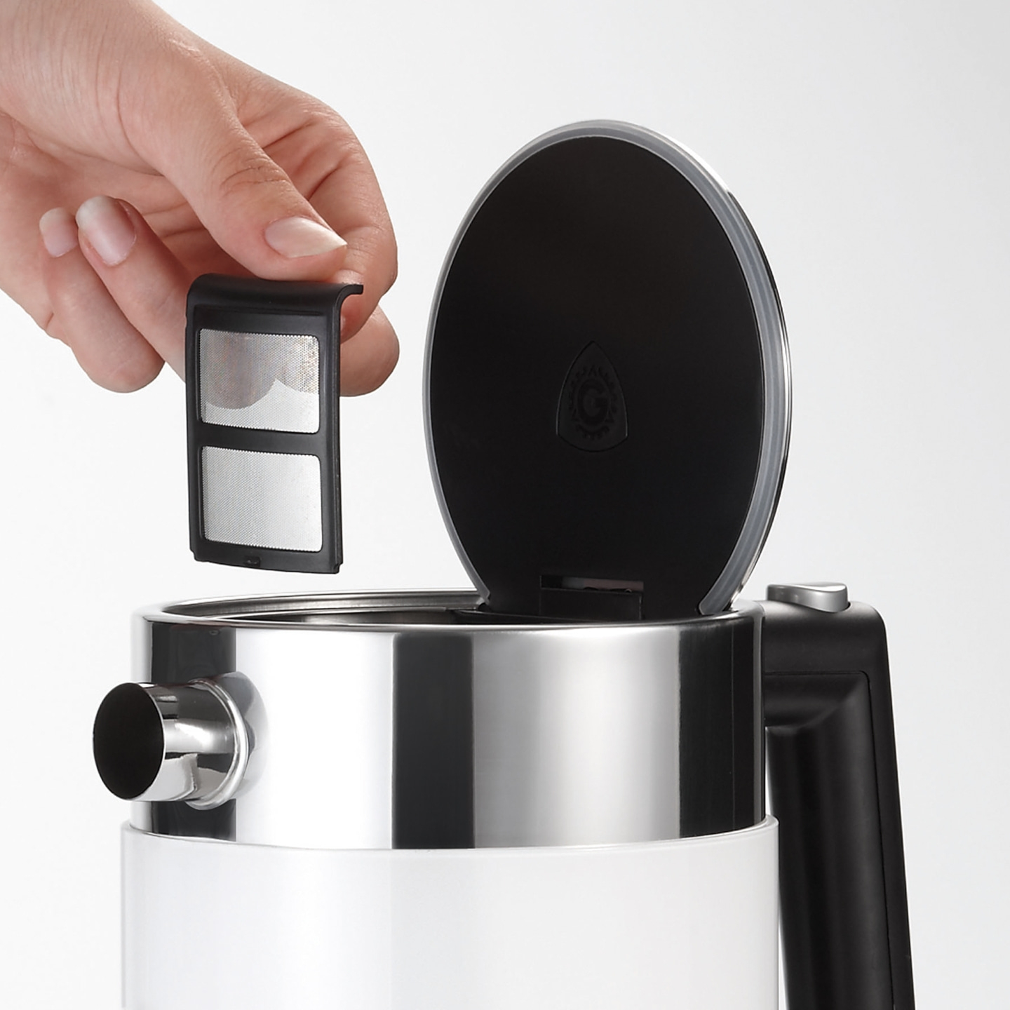 Hand holding filter over kettle. Black lid open. Stainless steel and white.