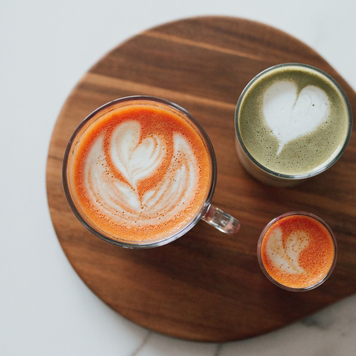 Trois boissons avec latte art sur une planche en bois, vue de dessus.