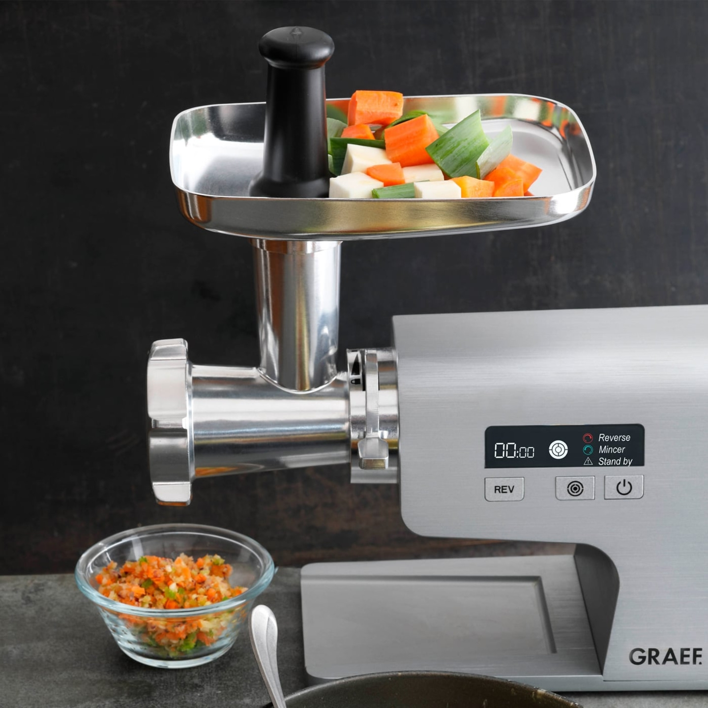 Meat grinder with vegetables, bowl of chopped vegetables, GRAEF logo on the side.