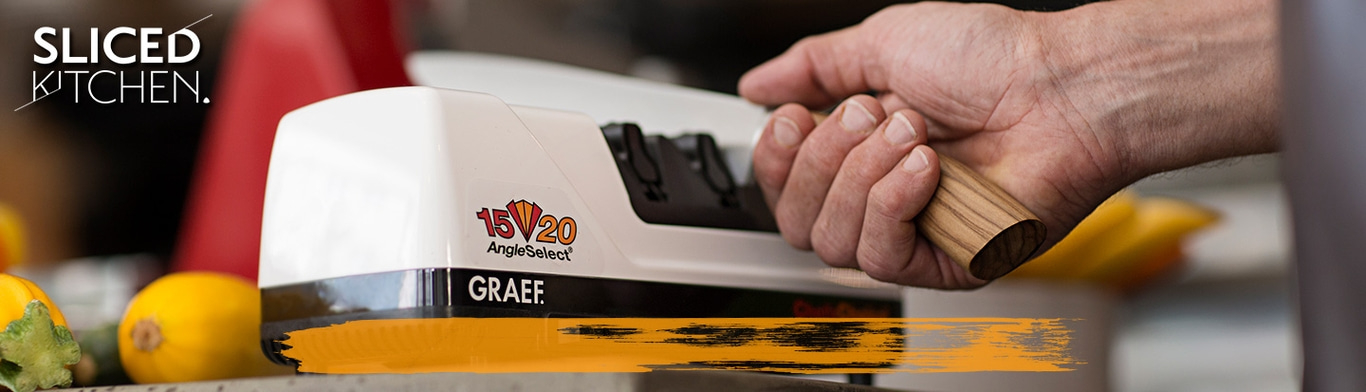 A man sharpens a knife with an electric knife sharpener in the kitchen.