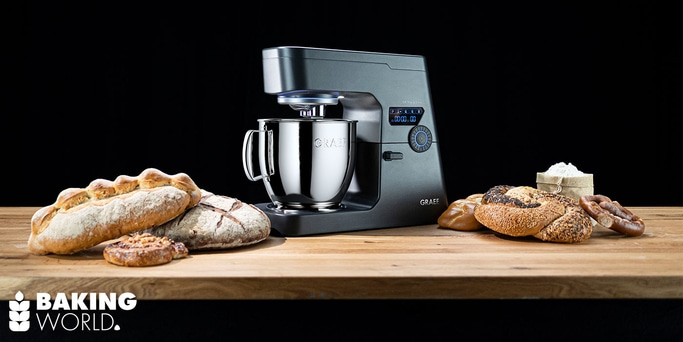 Kitchen machine with bread on wooden board against black background