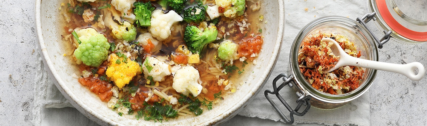 Soup with vegetables and spices in a bowl and a jar on a table