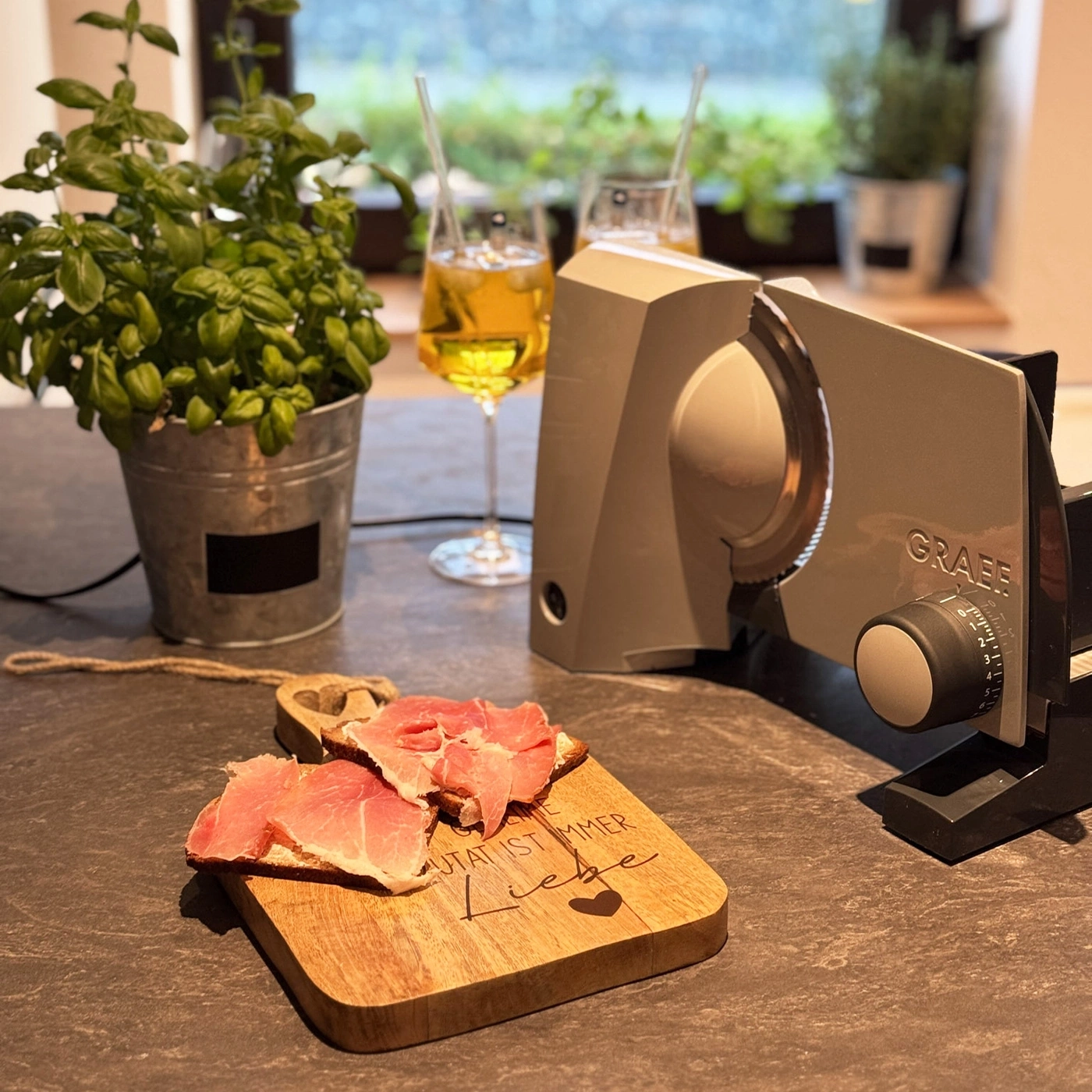 Une planche en bois avec du jambon dessus, à côté d'une trancheuse Graef.
