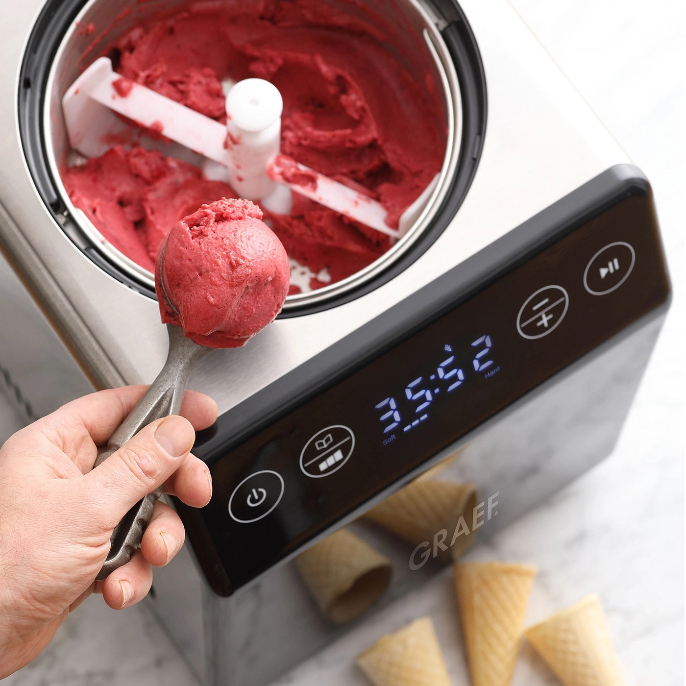 Ice cream machine with red ice cream, ice cream scoop, and waffle cones.