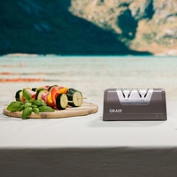 Vegetable skewers and knife sharpener on table with mountain landscape background