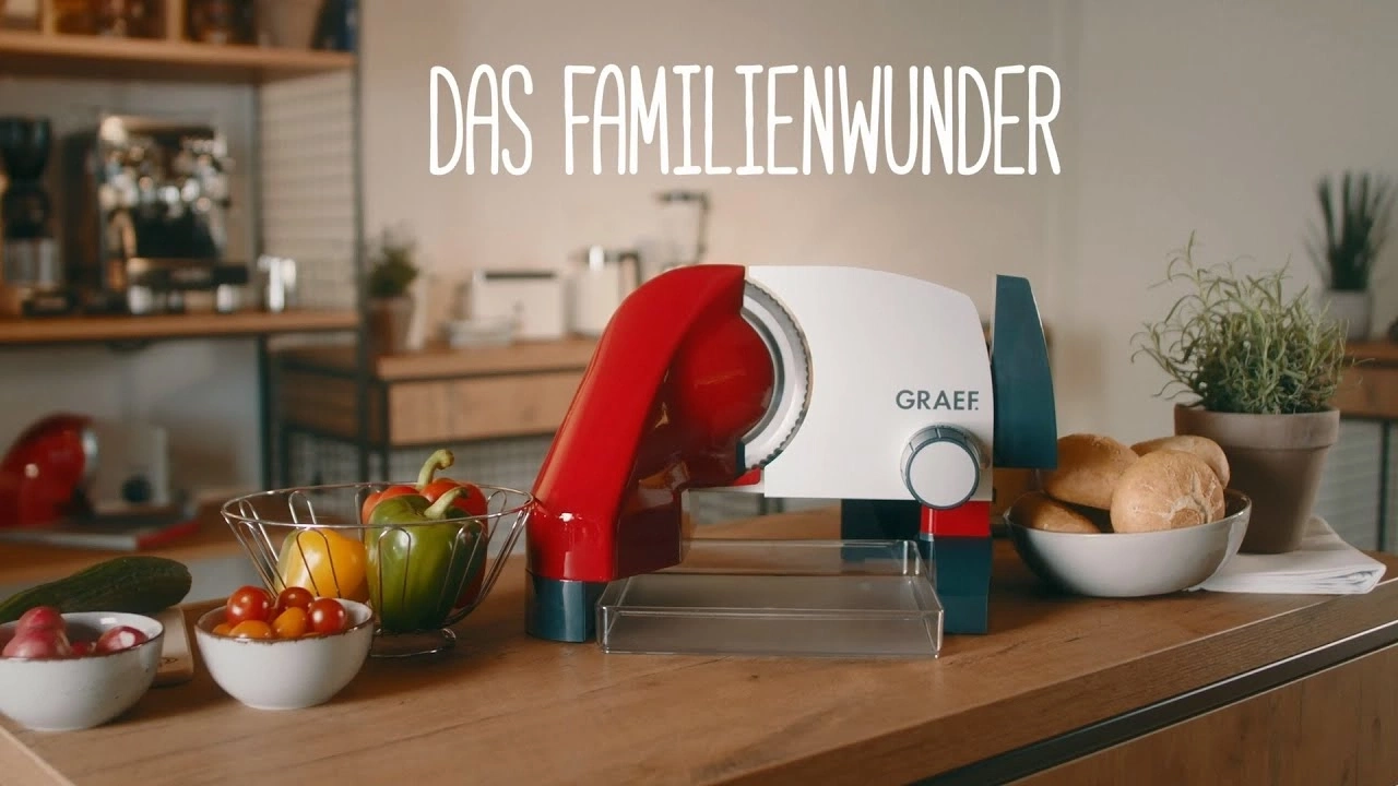 Scène de cuisine avec trancheuse, légumes et petits pains sur la table, 'DAS FAMILIENWUNDER'.