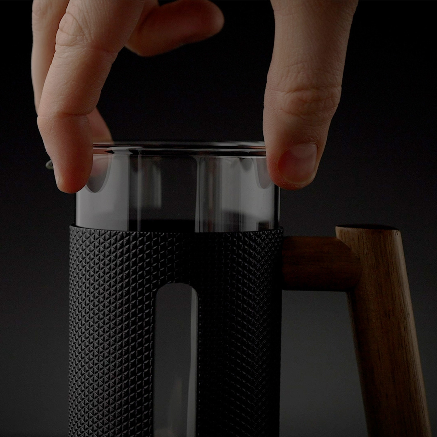 Primo piano di una mano che tiene un contenitore di vetro con manico in legno.