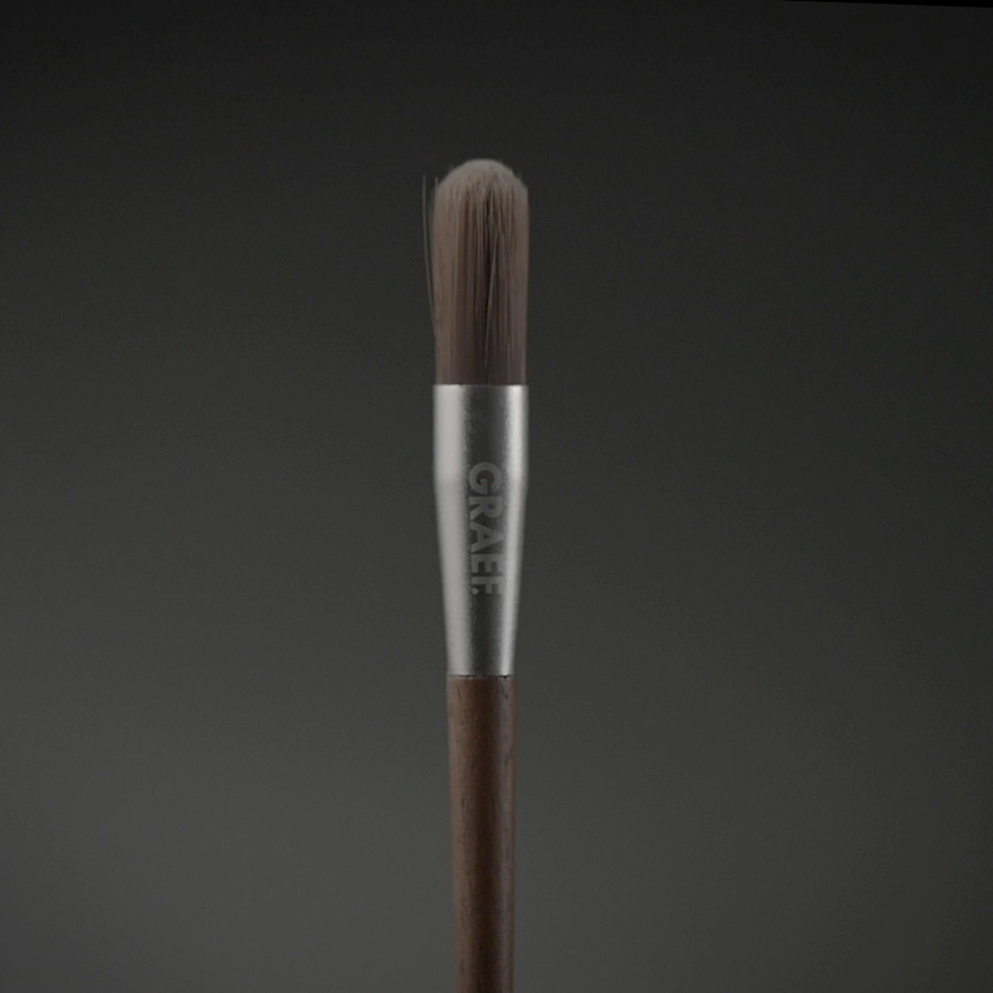 Un pinceau de maquillage avec un manche en bois et l'inscription argentée "GRAEF".