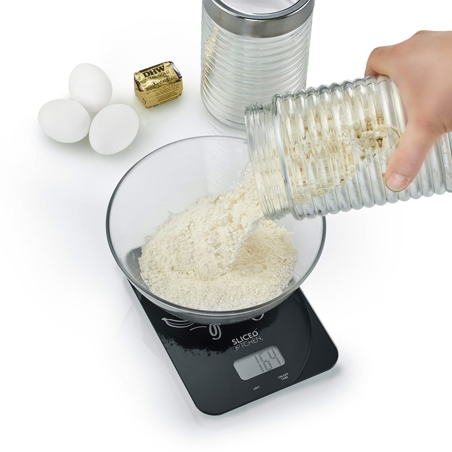 Flour being poured into a bowl on a scale, with eggs and butter in the scene.