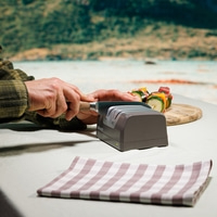 Man sharpening a knife with an electric knife sharpener on a table.
