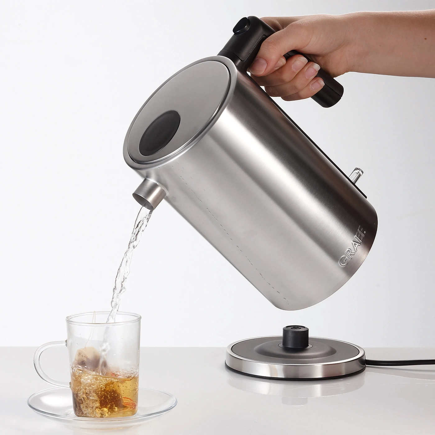 Una persona versa acqua da un bollitore in una tazza da tè con una bustina.