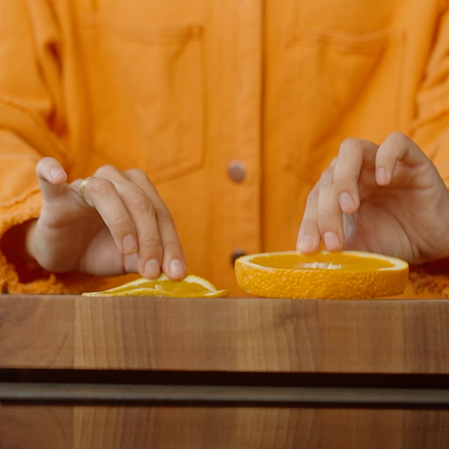 Person arranging orange slices on a wooden table, one thin and one thick slice.