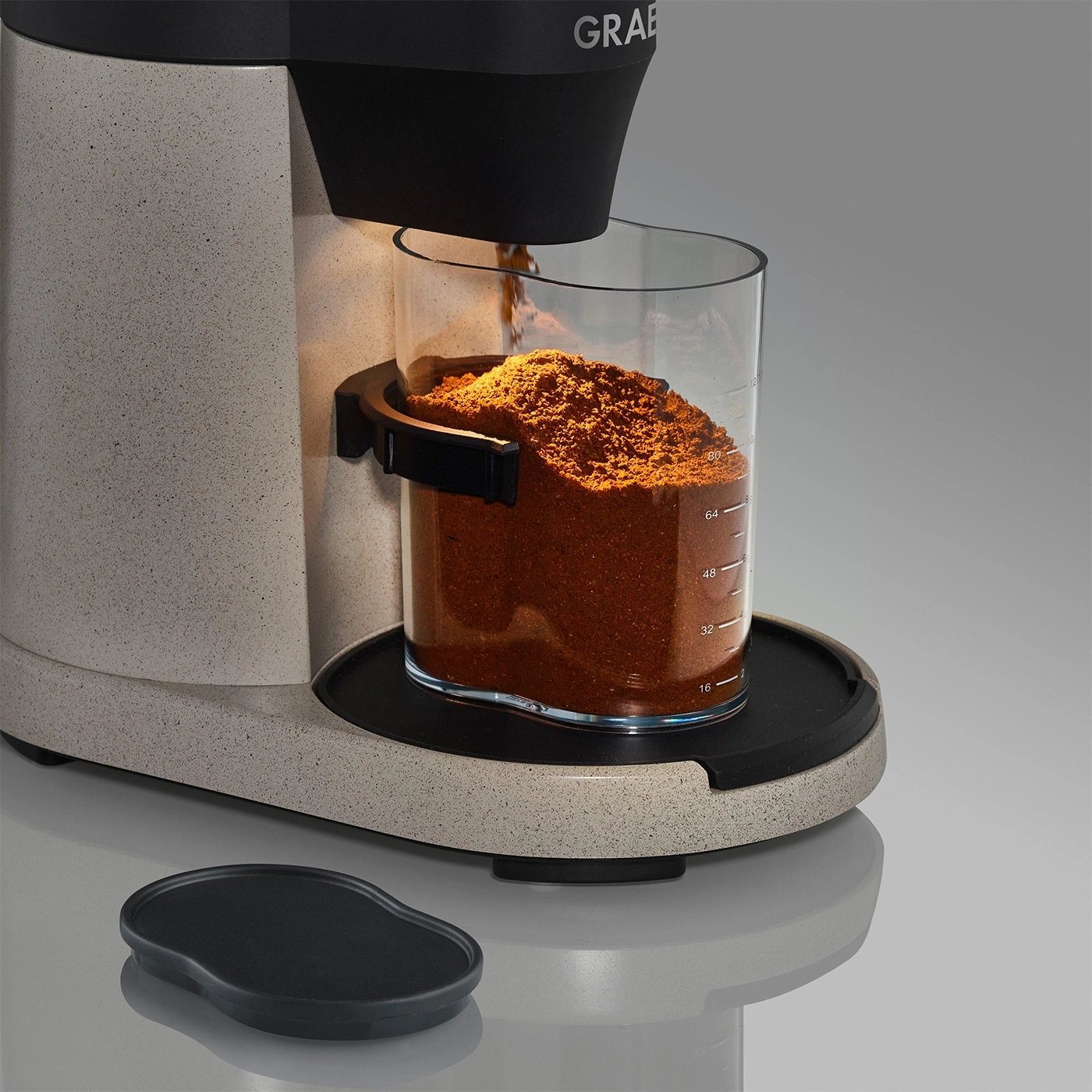 Macinacaffè con contenitore in vetro pieno di polvere di caffè e coperchio nero.