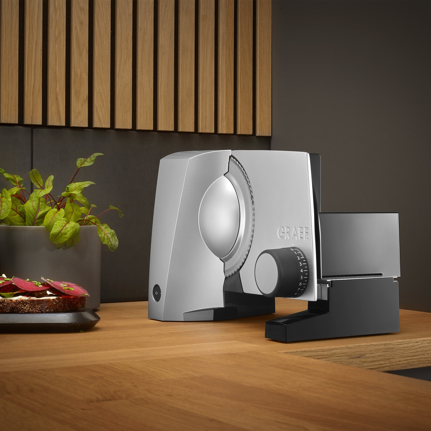 Graef slicer on wooden table with bread and plant in the background