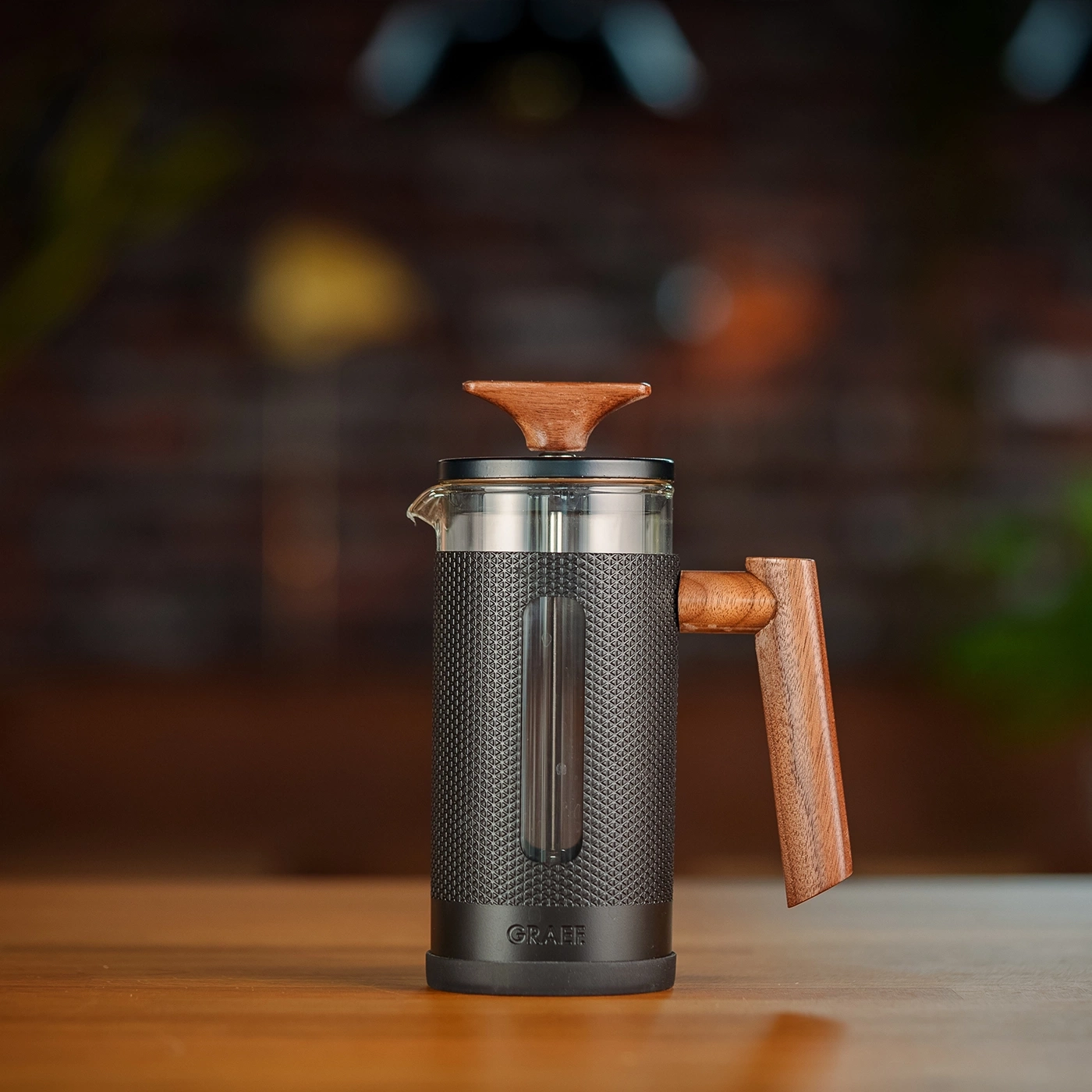 Primo piano di una caffettiera con manico e coperchio in legno su un tavolo di legno.