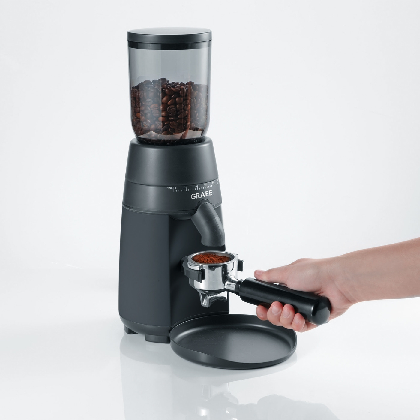 Coffee grinder with beans and powder, hand holding portafilter, black