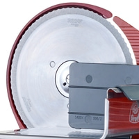 Close-up of a meat slicer with a sharp blade and a red housing, ready to slice.