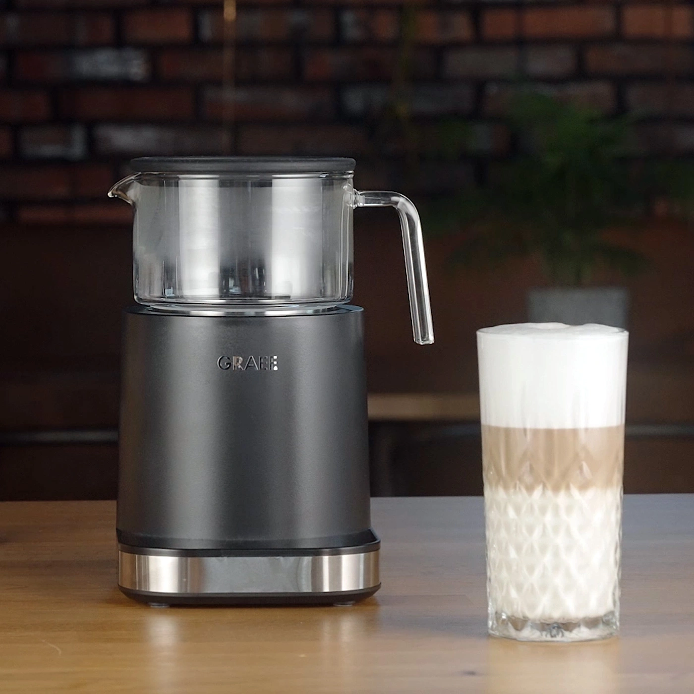 Milk frother with glass jug and a latte macchiato next to it.
