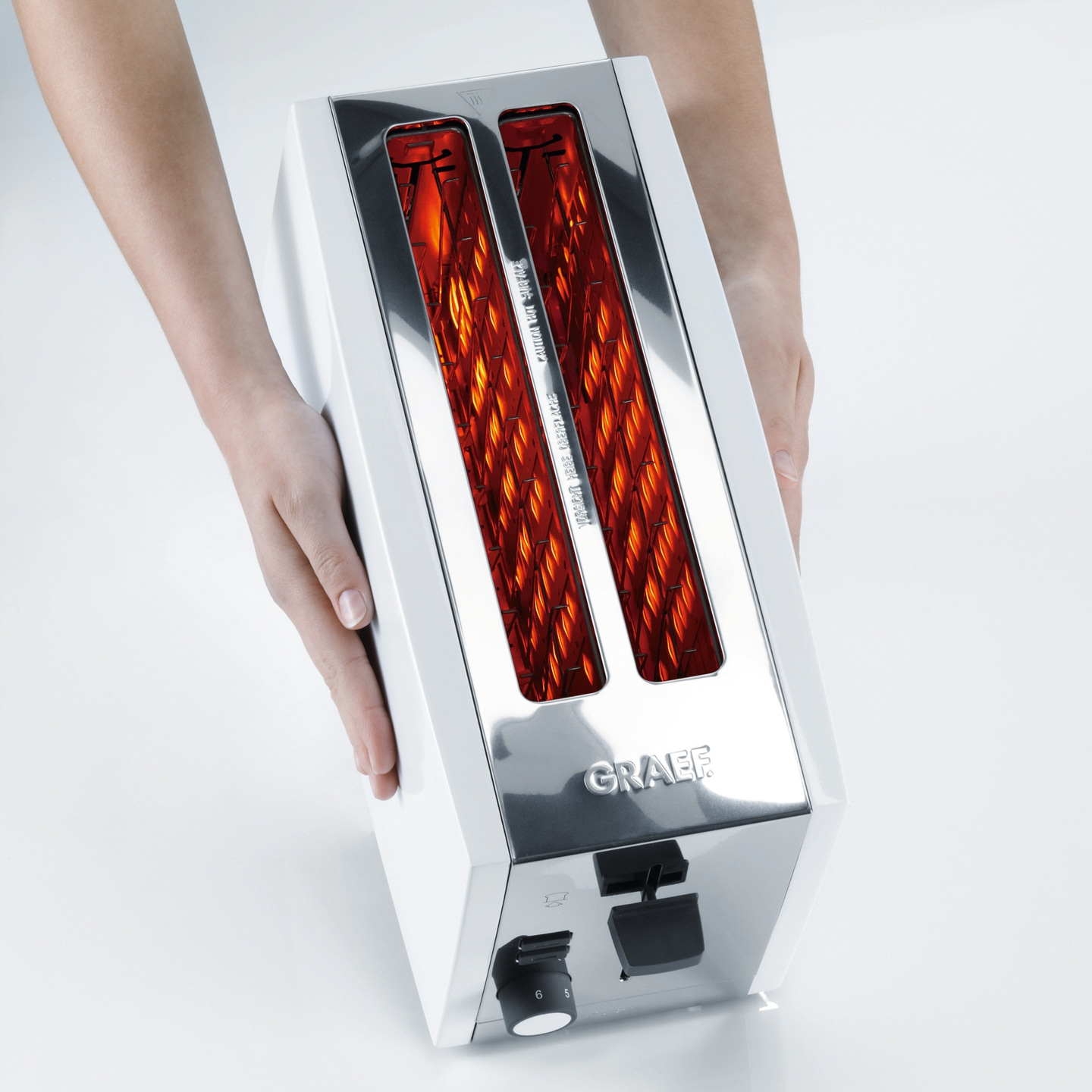Grille-pain tenu par des mains, blanc et brillant, avec lumière rouge à l'intérieur, marque GRAEF.