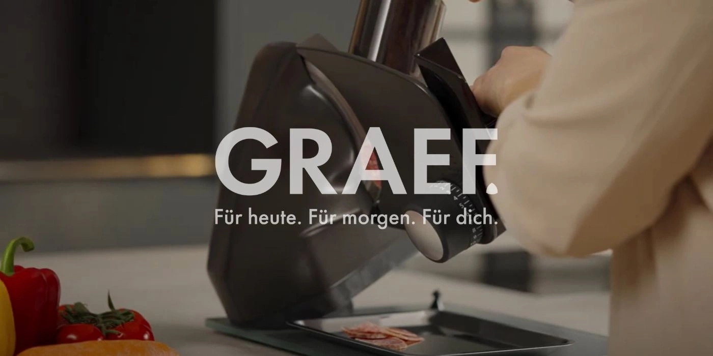 Pubblicità GRAEF: Persona che affetta salsiccia con un'affettatrice, testo: Per oggi. Per domani. Per te.