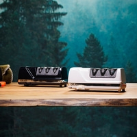 Two knife sharpeners, black and white, on a wooden table with a forest background.