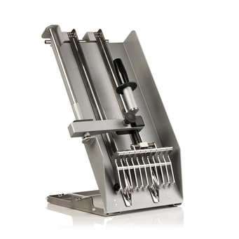 Machine argentée avec poignée et crochets, sur une surface blanche, vue en angle.