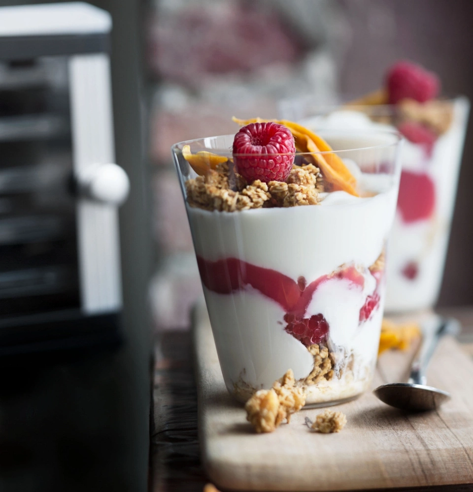 Dessert au yaourt avec framboises, granola et chips de mangue dans des verres sur planche