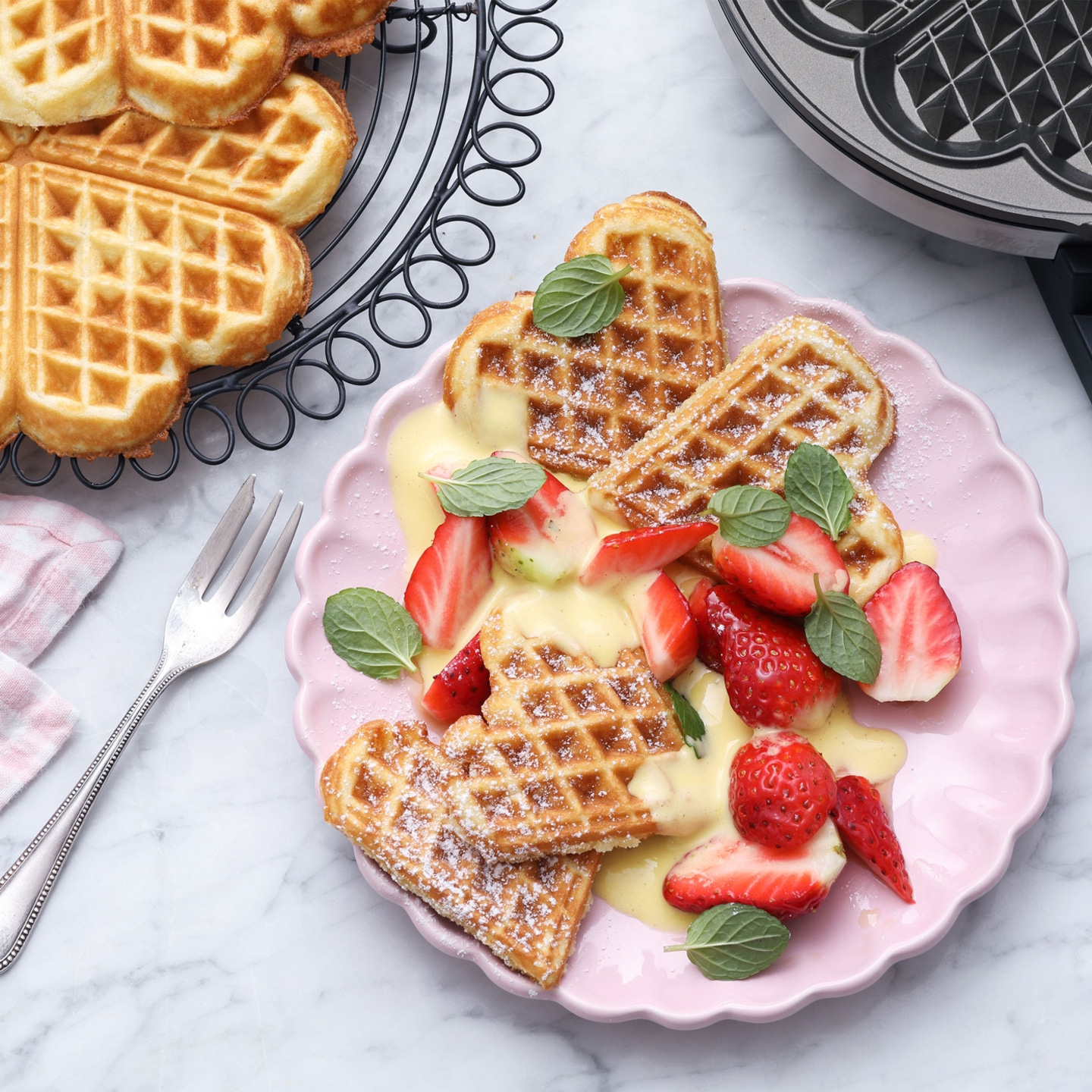 Heart-shaped waffles with strawberries and vanilla sauce on a plate.