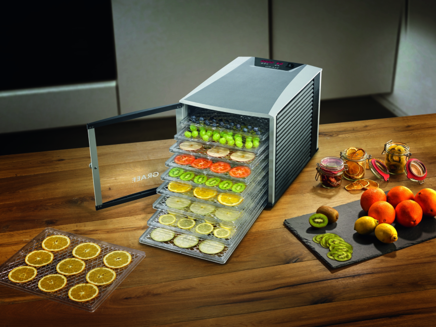 Food dehydrator with fruits, lemons, oranges, kiwi, grapes, blueberries, tomatoes.
