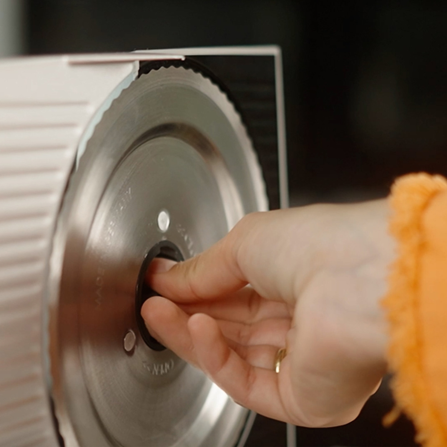A hand adjusts the blade of a meat slicer.