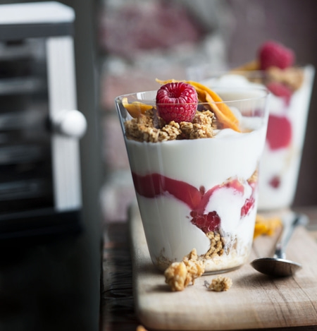 Yogurt dessert with raspberries, granola, and mango chips in glasses on a wooden board