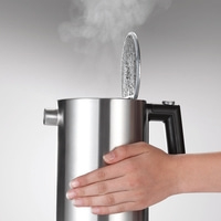 Stainless steel kettle with steam, open lid, hand, grey background, close up