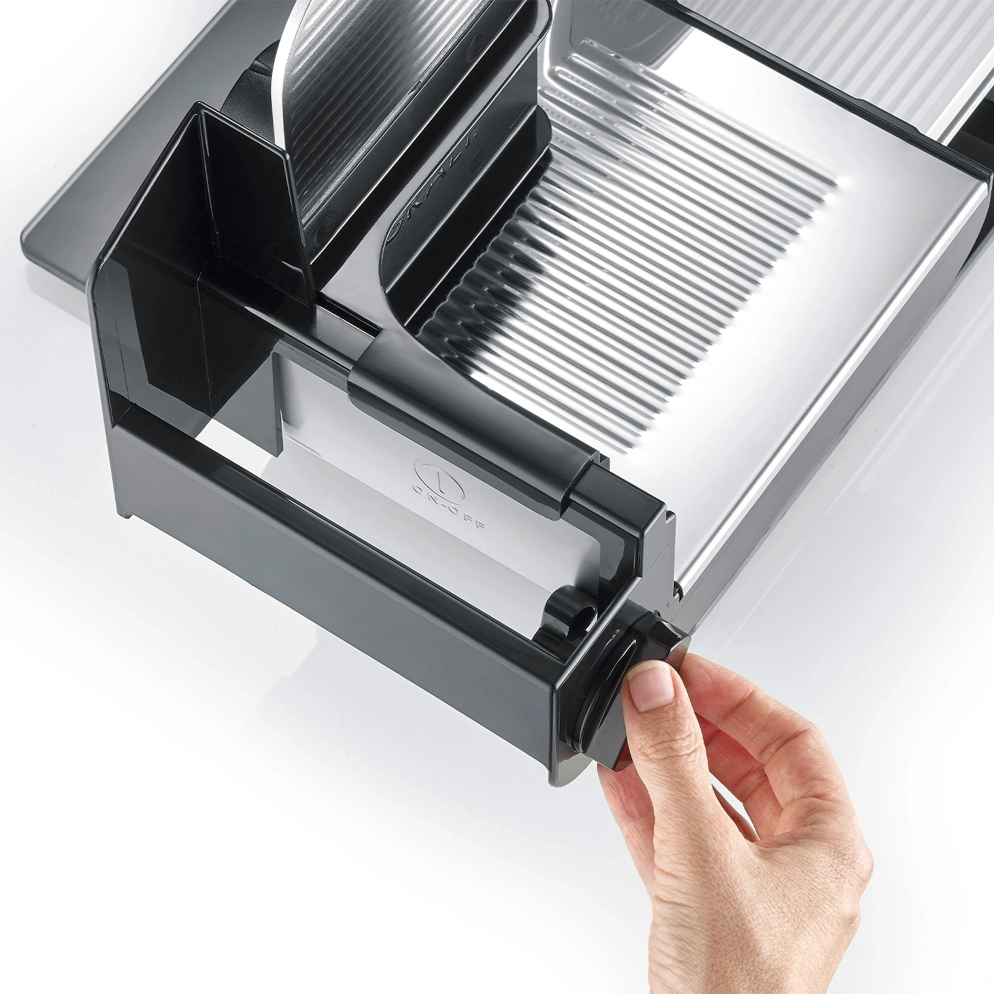Close-up of a black meat slicer with a hand turning a knob on a white surface
