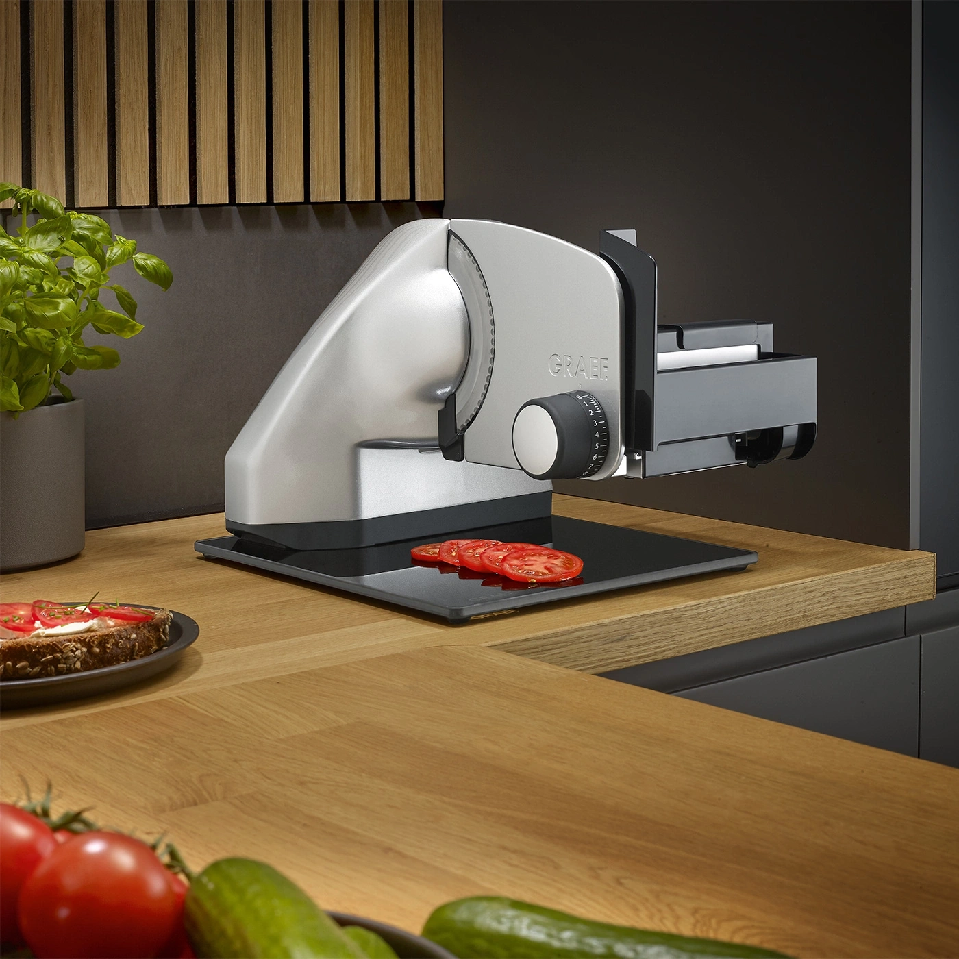 Affettatrice Graef con pomodori su superficie in legno e verdure in primo piano