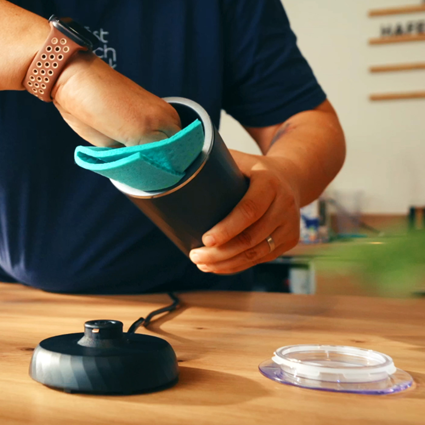 A hand cleans a black container with a blue sponge.