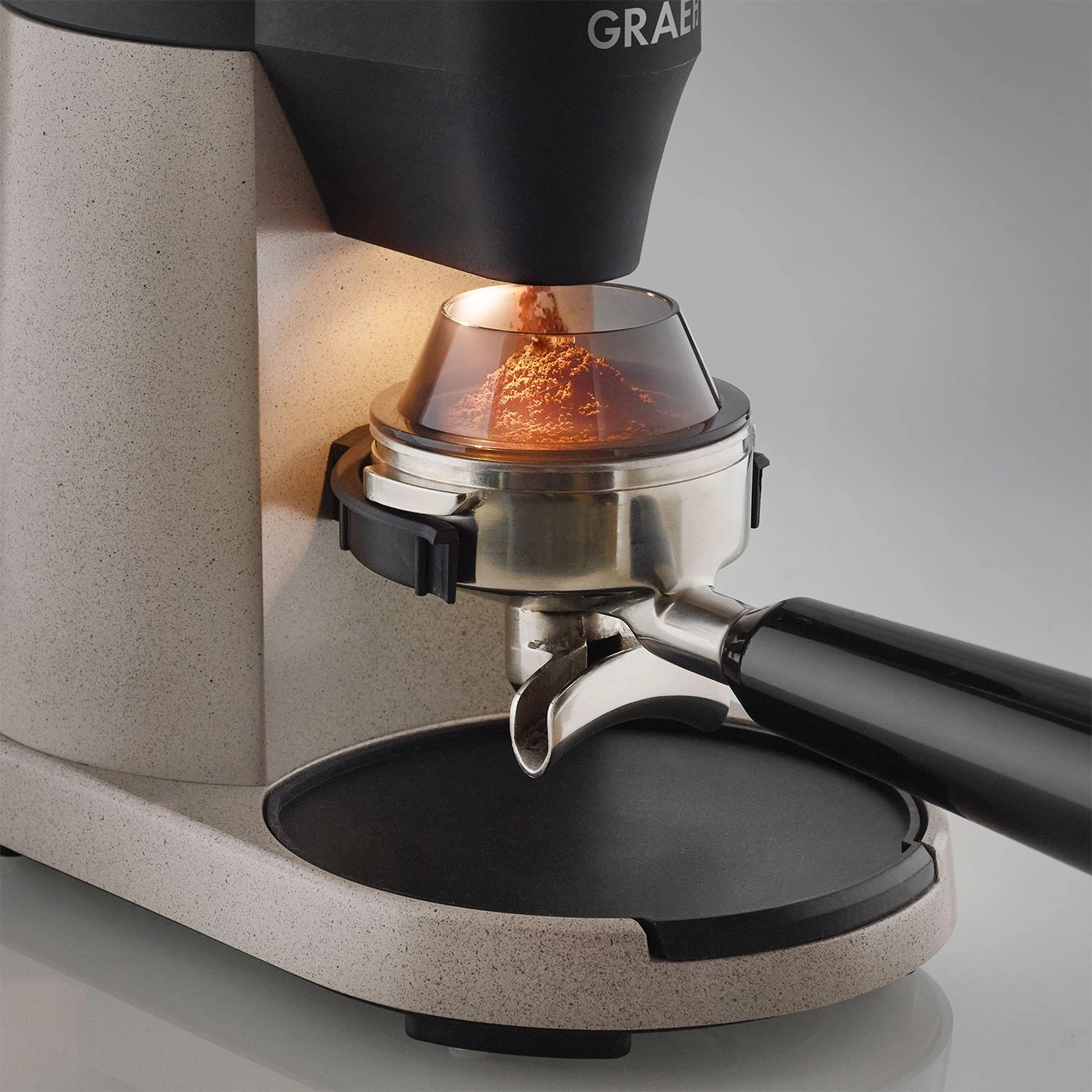 Primo piano di macinacaffè con polvere di caffè, illuminato, sfondo grigio