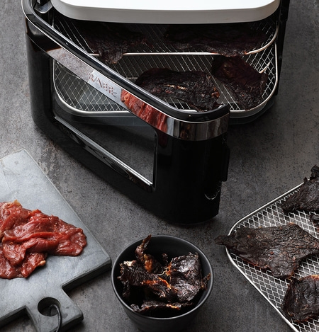 Meat dehydrator with meat and jerky on a gray surface, close-up shot