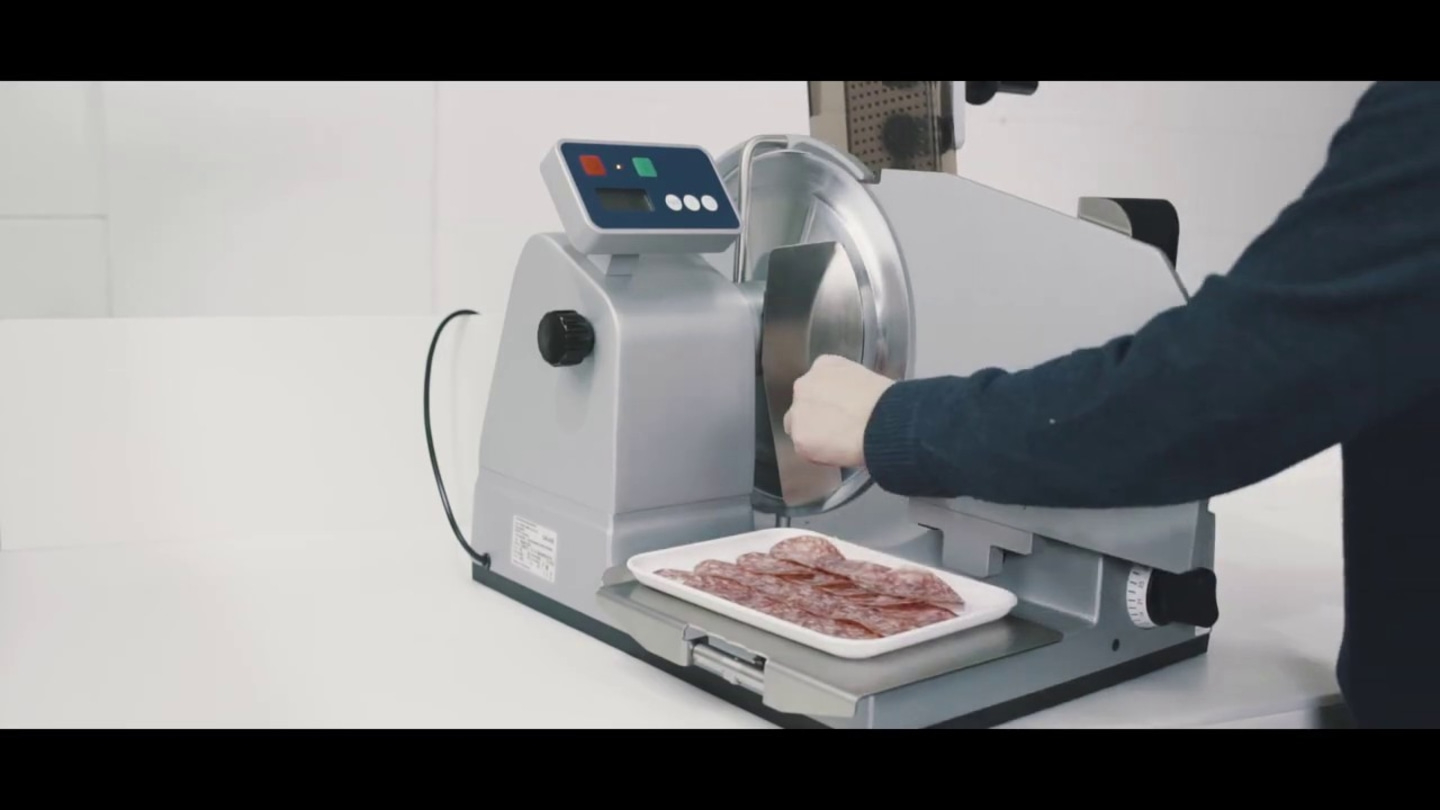 Affettatrice taglia salame. Persona usa la macchina. Fette su vassoio. Macchina argento.