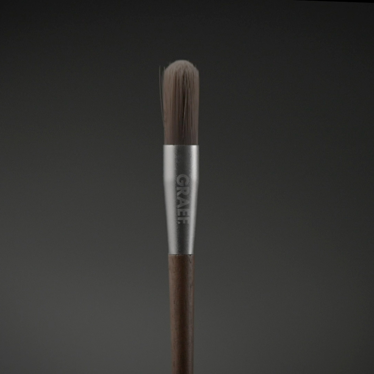 Un pinceau de maquillage avec un manche en bois et l'inscription argentée "GRAEF".